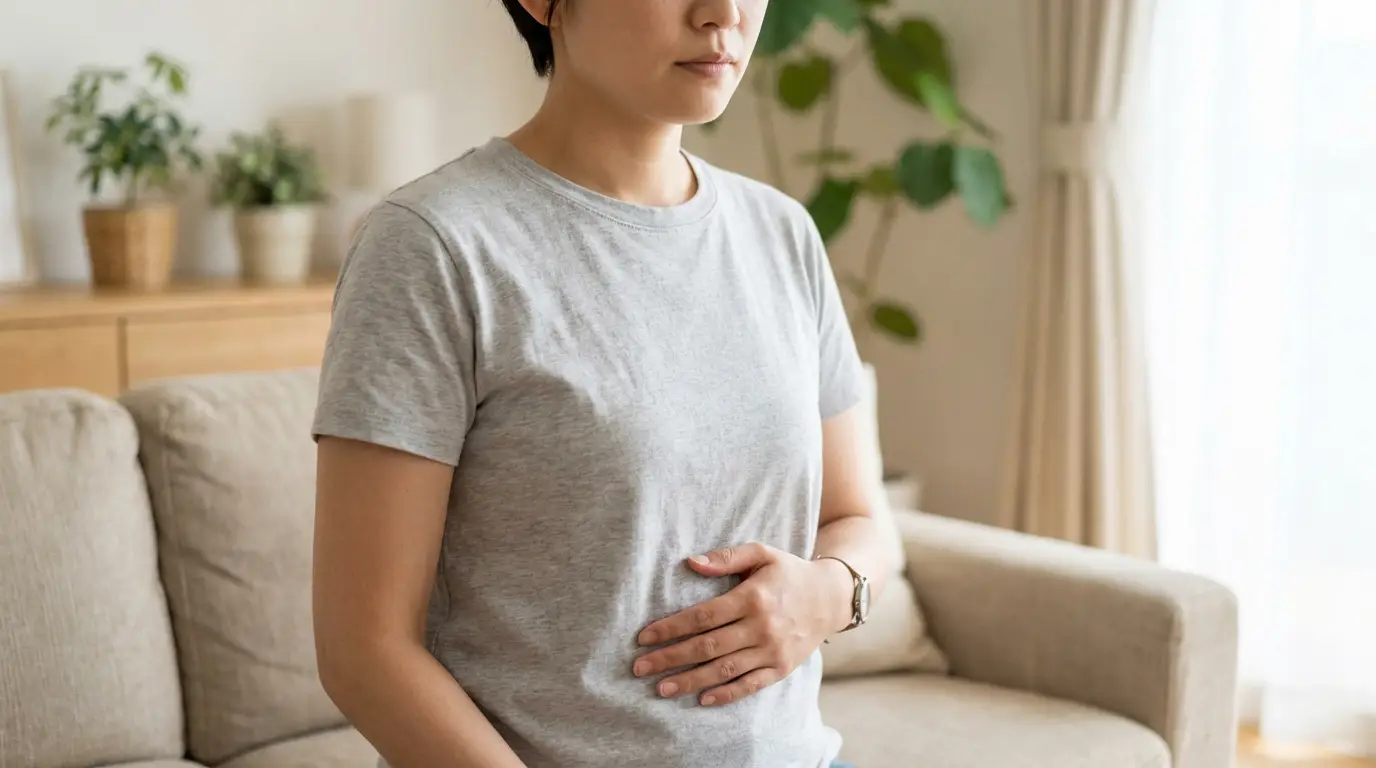 Ventre gonflé et dur : comprendre et soulager la distension Jeune femme assise sur un canapé, main sur le ventre, l'air soucieux, indiquant un ventre gonflé ou une gêne digestive.