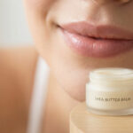 Gros plan d'une bouche souriante près d'un baume au karité et d'un stick SPF 30 pour le soin des lèvres.