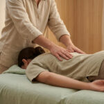 Une personne est allongée sur le ventre, recevant un massage Tui Na du dos par un praticien. Ambiance apaisante de bien-être.