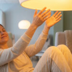 Une femme souriante, les yeux fermés, reçoit de la luminothérapie dans un fauteuil confortable, mains levées vers la lumière.